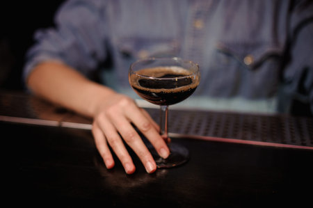 Bartender girl holding a cocktail glass with brown alcohol standing on the bar counterの写真素材