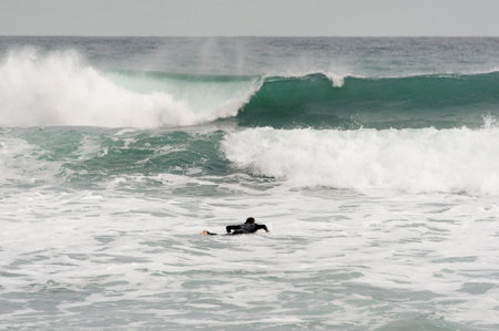 Brunette guy in the black swimsuit lying on a white surf on the stormy ocean.