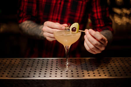 Barman decorating fresh juicy cocktail with orange and cherryの写真素材