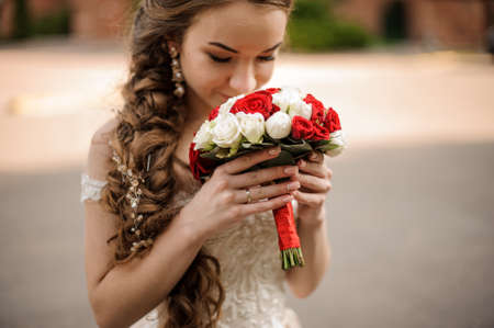 Happy bride in a wedding dress with a braid hairstyle sniffing a bouquet of rosesの写真素材