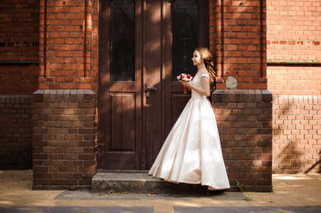 Young and beautiful bride in white wedding dress standing near the wooden doorの写真素材