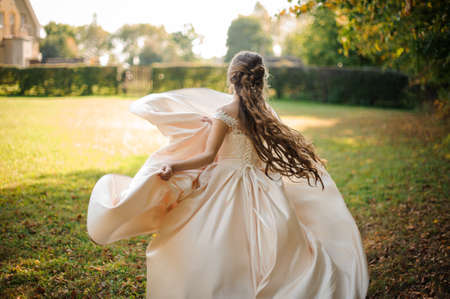 Back view of a beautiful bride spinning in a wedding dress dancing on the green fieldの写真素材