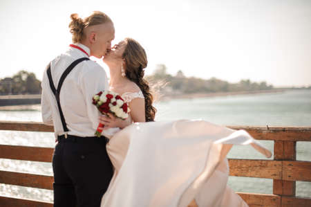 Happy married couple kissing on the wooden bridge in background of the seaの写真素材
