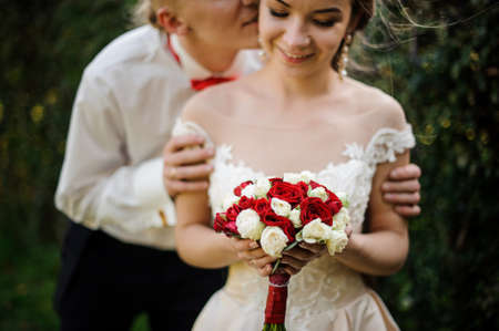 Groom kissing his young and beautiful bride in background of green treeの写真素材