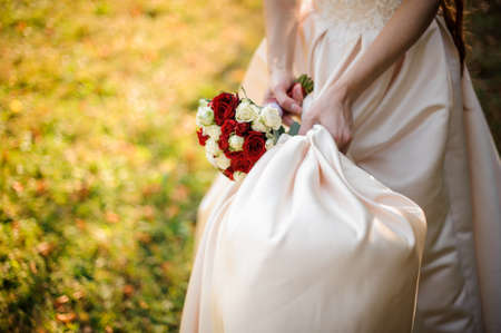 Bride hand holding a wedding dress and bouquet of flowersの写真素材