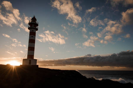 High striped white and red lighthouse in the background of rising sunの写真素材