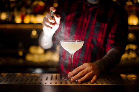 Barman sprinkling elegant cocktail glass with alcoholic drink with bitterの写真素材