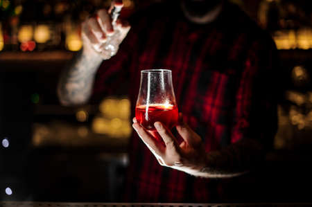 Tattooed barman sprinkling bitter into the glass with red sweet cocktailの写真素材