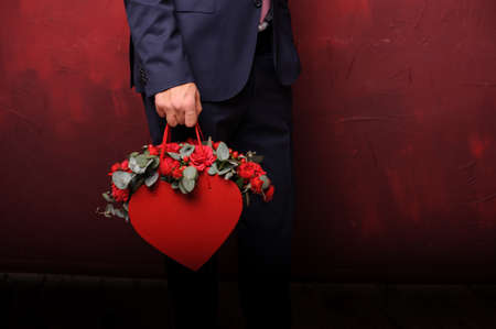 Man holding in a hand red box of beautiful flowers standing on the background of the dark wallの写真素材