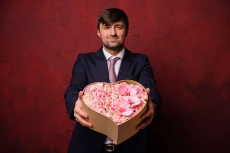 Man holding in a hands a box of pink flowers standing on the background of the dark wallの写真素材
