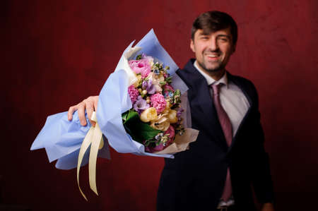 Smiling man holding in a hands a bouquet of beautiful pastel colored flowersの写真素材
