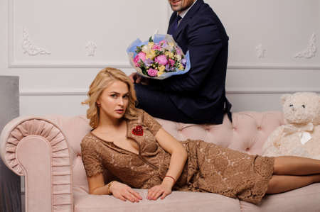 Beautiful girl in the beige dress lying on the couch and man sitting up the herの写真素材