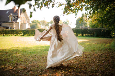 Beautiful bride in a white wedding dress running in the autumn parkの写真素材