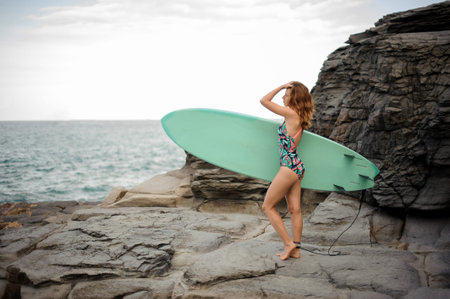Side view of a beautiful girl in the multi colored swimsuit standing with the blue surf on the...