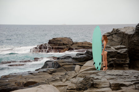 Beautiful girl in the multi colored swimsuit standing with the surf on the rock beach of Atlantic...