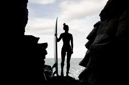 Silhouette sporty girl in the swimsuit standing with the surf inside the rock on the beach Atlantic ocean on the background of clear skyの写真素材