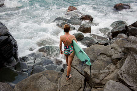 Rear view girl in the multi colored swimsuit standing with the surf looking at oceanの写真素材