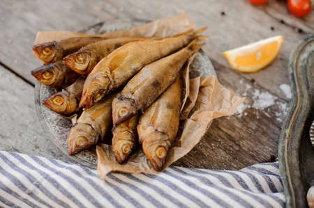 Smoke-dried fish on plate on a baking paper on the grey striped napkin with a salt and lemonの写真素材