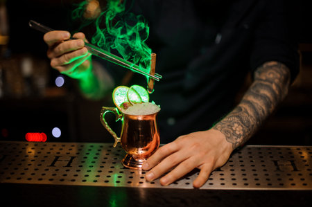 Bartender adding to a cocktail in the cooper glass with a dried orange aromatic smoked cinnamon with...