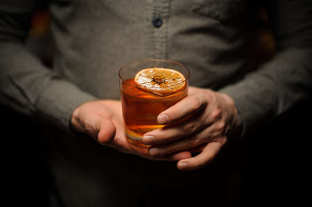 Bartender holding a delicious cocktail with a dried orangeの写真素材