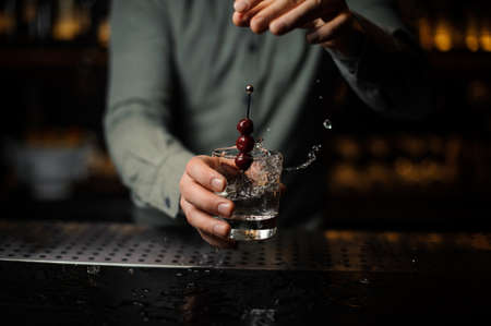 Bartender throwing into a cocktail glass a berries on a skewerの写真素材