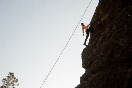 Girl equipped with a rope climbing on the sloping rock and looking downの写真素材