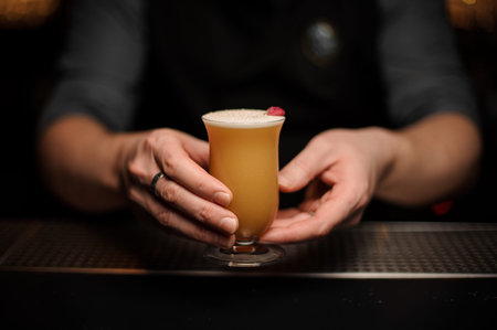 Bartender serving a cocktail in the glass with foam decorated with a one red rose bud