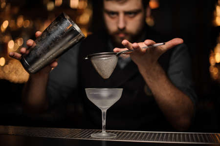 Professional bartender pouring cocktail from the shaker through the special sieveの写真素材