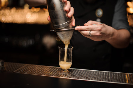 Professional bartender pouring cocktail from the steel shaker through the sieveの写真素材