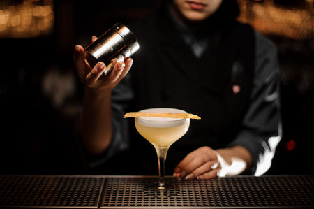 Professional bartender girl holding a spice shaker adding to a delicious cocktail