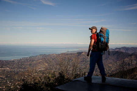 Strong man with a backpack standing and looking on the mountainsの写真素材