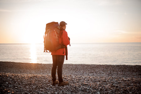 Man with a backpack standing and looking at the sea