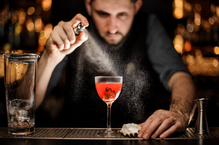 Professional male bartender spraying on the delicious transparent red cocktail in the glass on the...