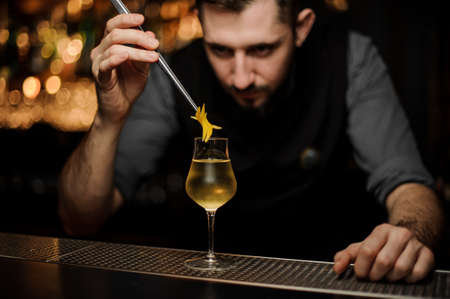 Bartender adding to a cocktail in the glass a lemon zest with tweezersの写真素材