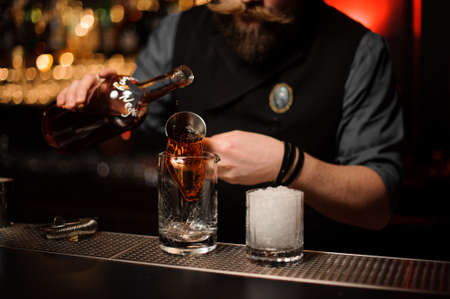 Bartender pouring a delicious brown cocktail from the steel jiggerの写真素材
