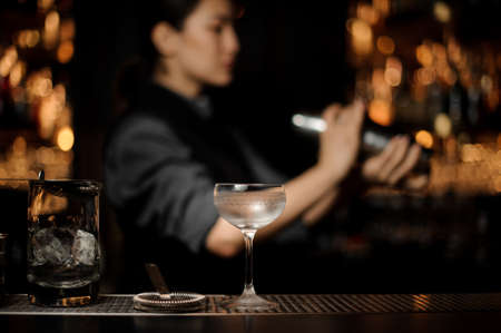 Cocktail glass on the blurred foreground of bartender girl holding a steel shakerの写真素材