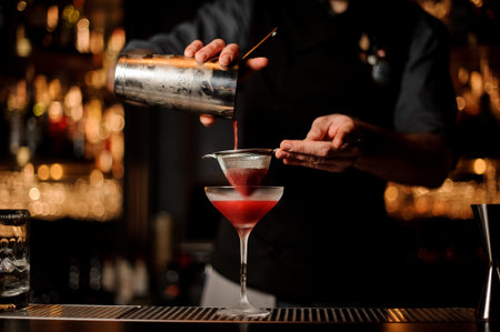 Professional bartender pouring a pink cocktail through the sieve to the glass
