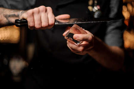 Bartender cutting a big ice cube with a knifeの写真素材