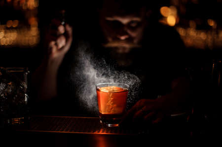 Bartender spraying to the cocktail glass with one big ice cube in the darkの写真素材