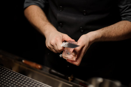 Bartender making an appropriate form to the ice cube with the special knife