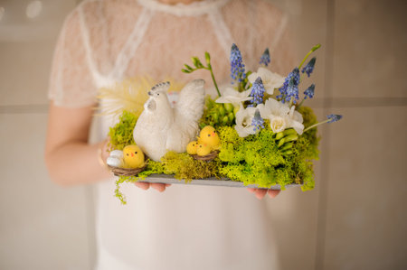 Girl holding a spring composition with toy chiken and white and blue flowers