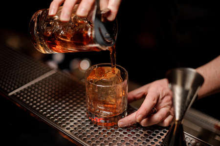Bartender pouring alcohol cocktail using glass with strainerの写真素材