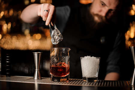 Bartender adds ice in glass with special ice tongs