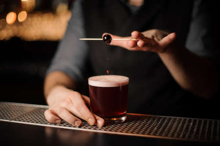 Bartender decorating alcohol cocktail with cherry on toothpickの写真素材