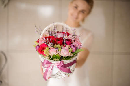 Smiling girl holding a spring white basket of red and pink rosesの写真素材