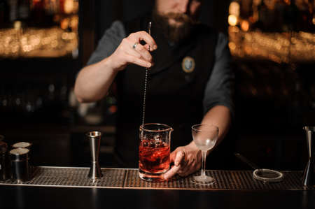 Barman stirring a red cocktail with a steel spoon in the measuring glass cupの写真素材