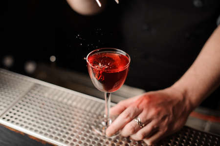 Professional bartender adding a decor of one red berry with tweezers to the cocktailの写真素材