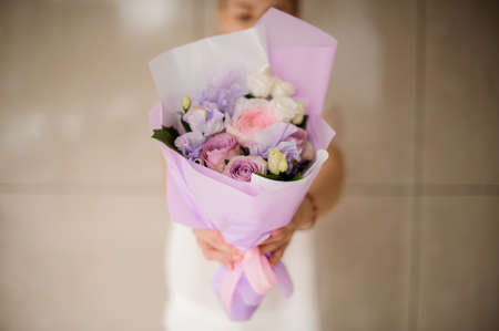 Woman holding a spring bouquet of tender violet and pink roses decorated with green leaves in paperの写真素材