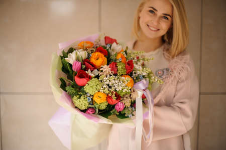 Smiling girl holding a bouquet of tender red, orange and green flowersの写真素材