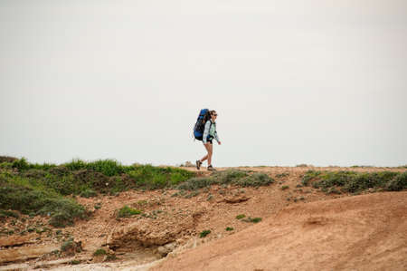 Young girl walking on the coast in shirt and sunglasses with a backpackの写真素材